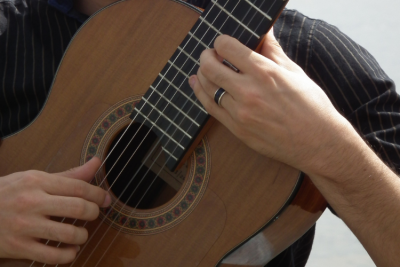 Closeup of acoustic guitarist's hand on the guitar fretboard.